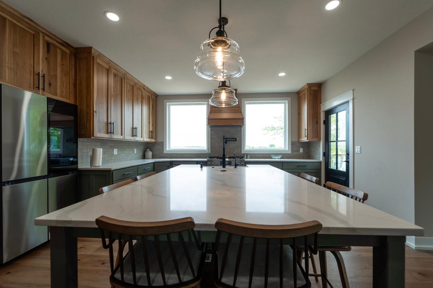 A finished kitchen with hickory upper cabinets, sage-green bases and a large waterfall quartz island