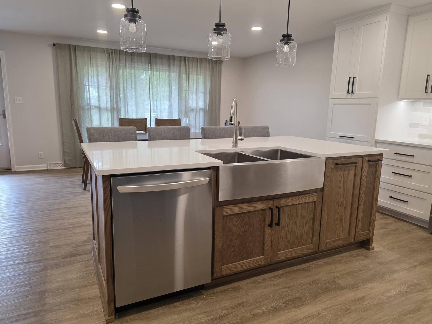 An oak island with a stainless farmhouse sink and white perimeter cabinets