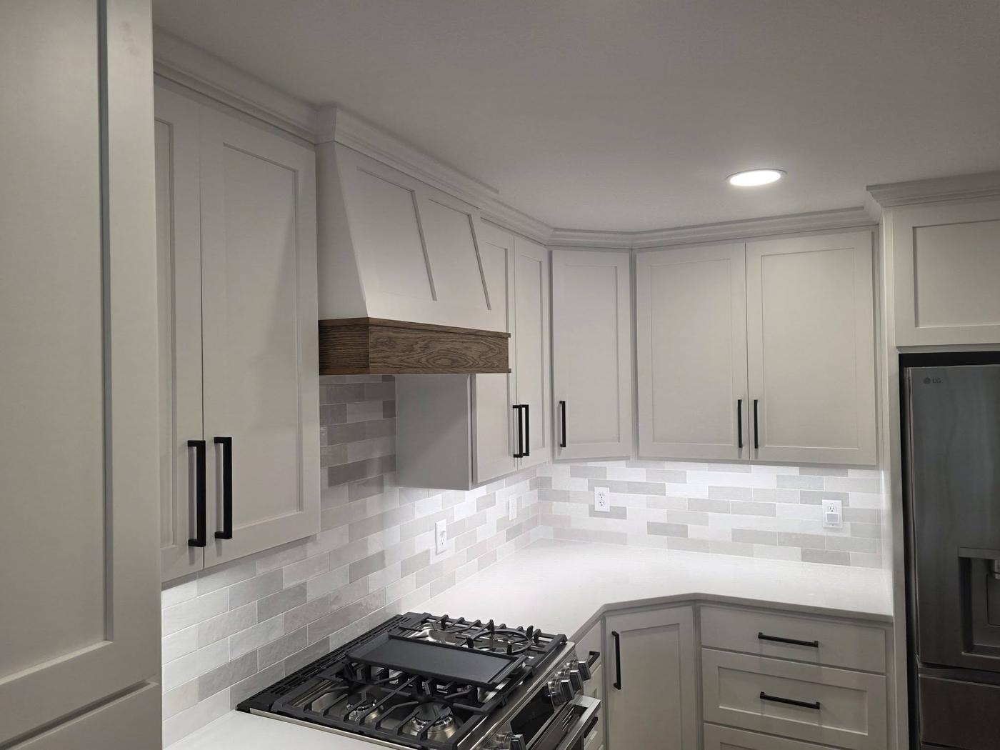 A white kitchen with a built range hood banded in oak