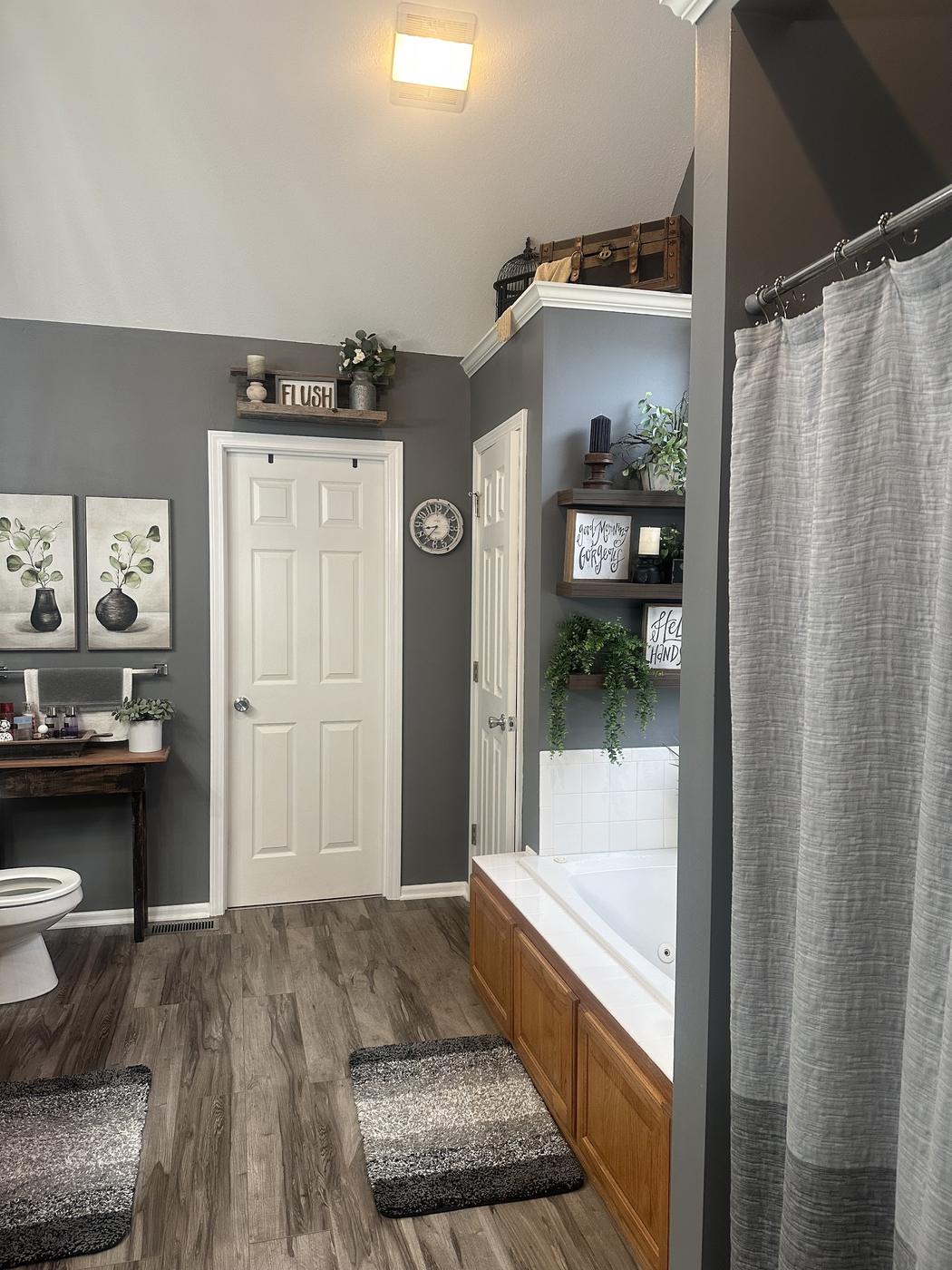 A dated bathroom with grey walls, an oak tub surround and a shower curtain