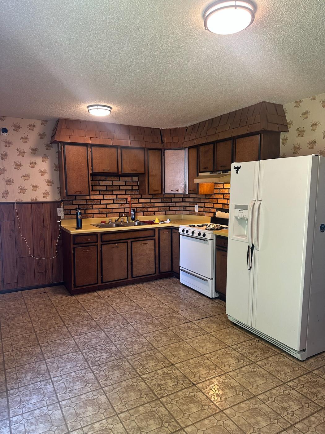 A dated kitchen with dark wood cabinets, brick-pattern backsplash and yellow laminate counters